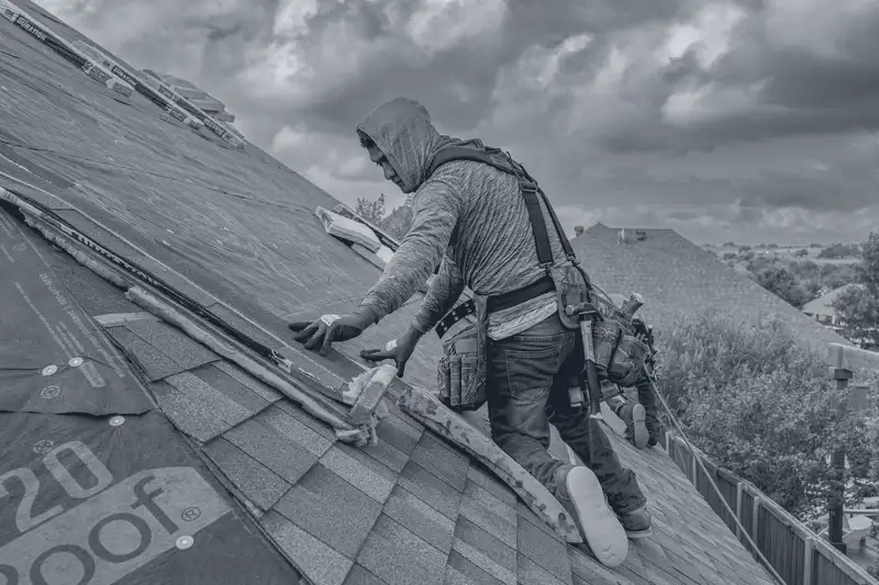 Two roofers laying asphalt shingles on a house roof under a clear sky