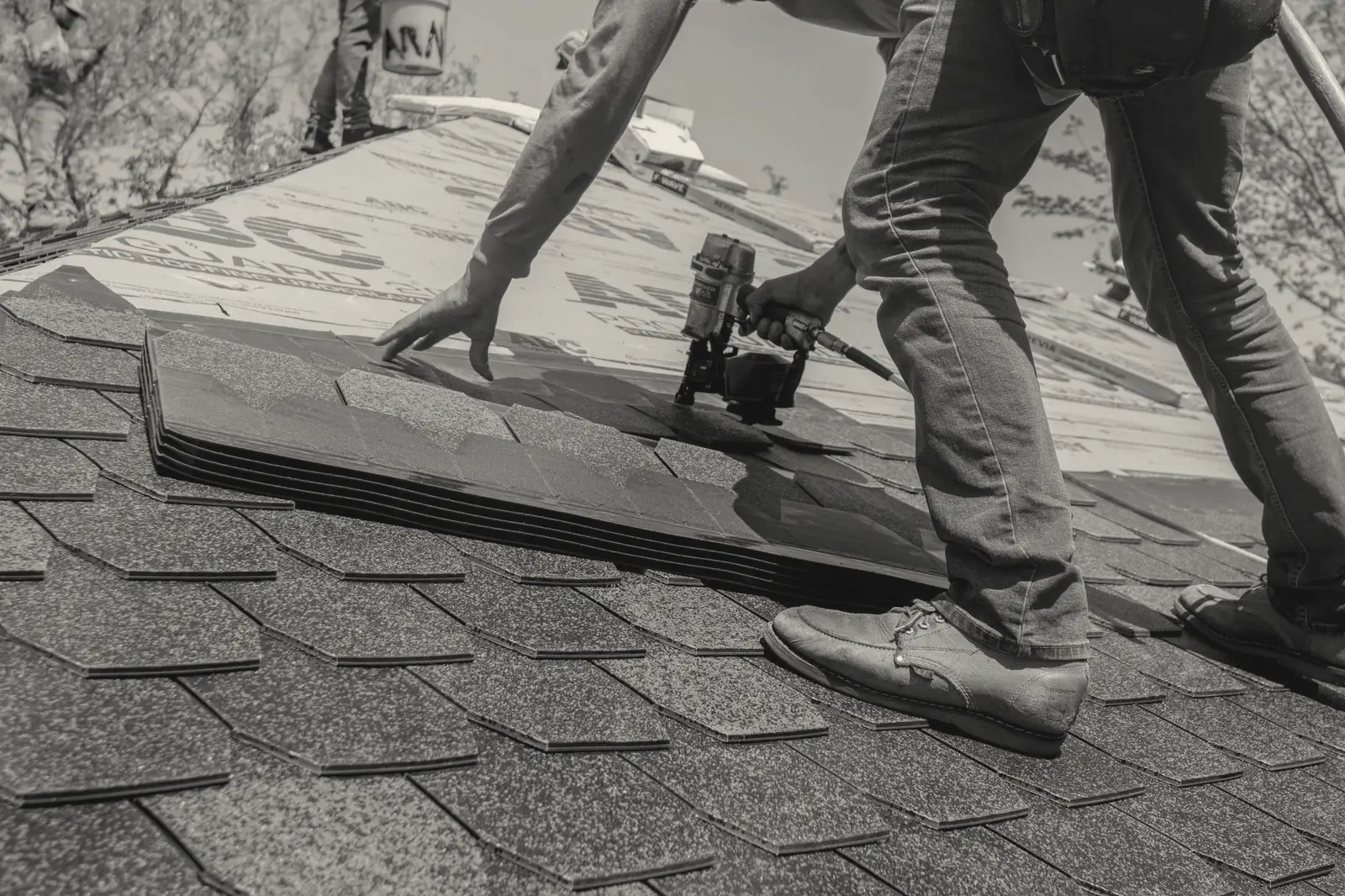 A roofer's nail gun driving into new asphalt shingles in hard sunlight